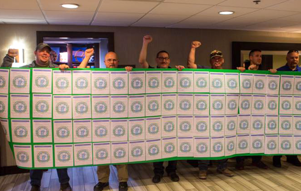 EMS Local 2960 members hold up copies of a petition joined together to form a large banner